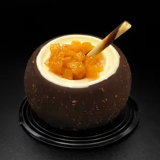 Coconut-shaped mousse dessert with coconut jam, mango chunks, and chocolate shell